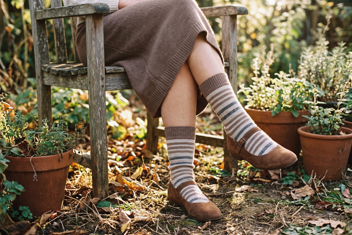 Calcetines altos de rayas de lana y cashmere en beige y gris con merceditas de ante, sentada en una silla de madera en el jardín