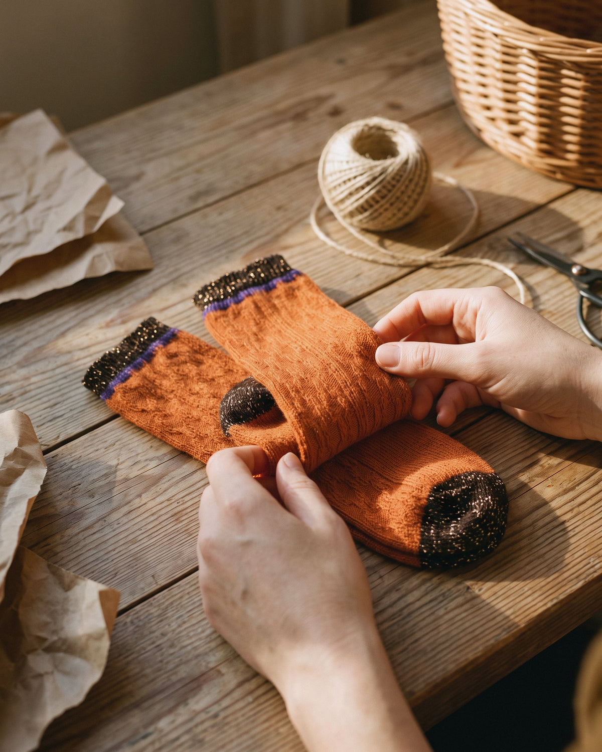 Manos doblando unos calcetines de lana suave con contraste color calabaza sobre una mesa de madera